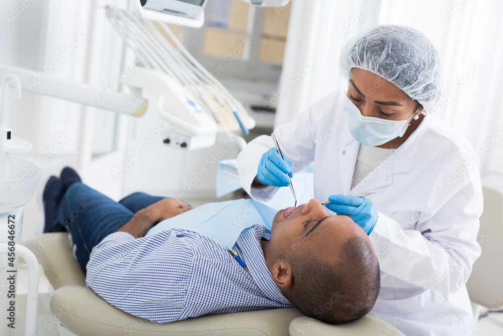Obraz premium Professional woman dentist performing teeth treatment to adult man in dental clinic