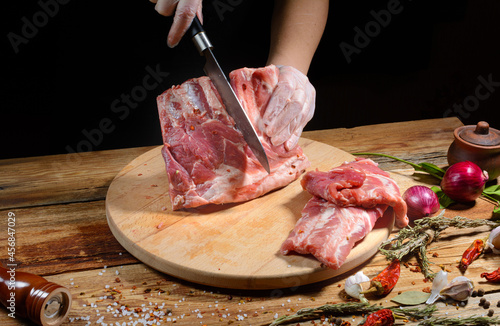 The chef uses his hands to slice pork ribs with a knife on a wooden cutting table. Selective focus. The concept of the cooking process.