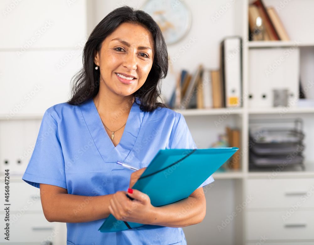© JackF - Polite latina female health worker meeting patient in medical office, filling out medical form at clipboard