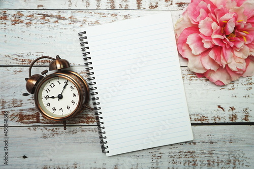 Notebook with blank pages withh alarm clock and floweron wooden background photo