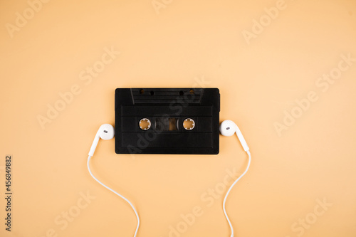 Stereo sound headphones and black cassette tape on pastel orange background.