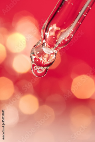 Pipette with serum on a red holiday background with bokeh.