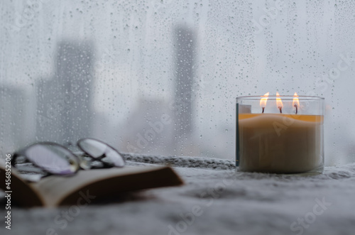 Burning aroma candle puts near by window that have rain drop in monsoon season with blurred city background. Zen and relax concept.