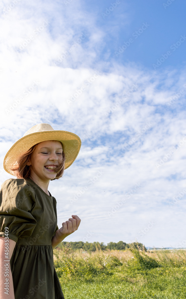 Girl in a linen dress and a straw hat laughs on a flower field. Wicker basket in hands. Wellness and freedom concept