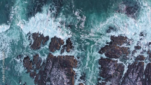 Aerial footage of waves washing onshore of rocky coast line. Moody turquoise ocean breaking into white wash. photo