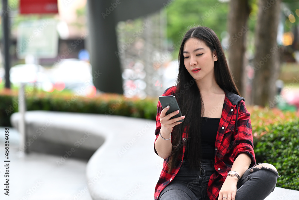 Young woman sitting outdoor in the city and using smart phone.