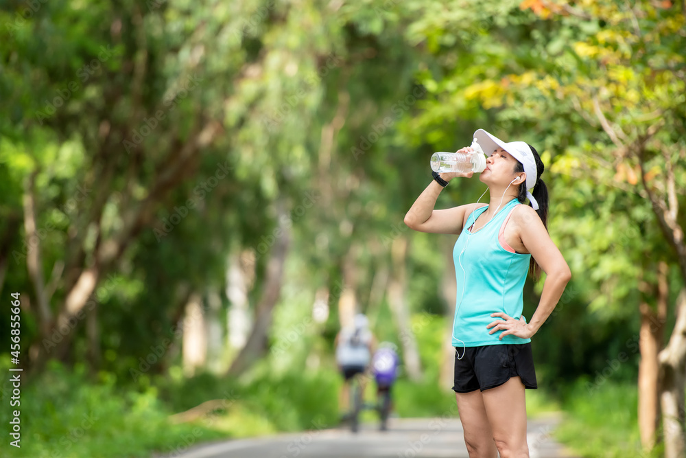 Healthy athletic asia woman is drinking pure water from the bottle refreshing herself after exercise in the nature park. Healthy and Lifestyle Concept