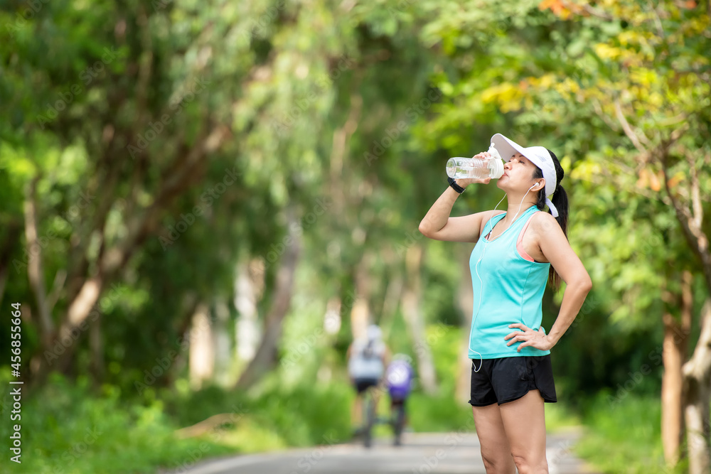 Healthy athletic asia woman is drinking pure water from the bottle refreshing herself after exercise in the nature park. Healthy and Lifestyle Concept Healthy athletic asia woman is drinking pure water from the bottle refreshing herself after exercise in the nature park. Healthy and Lifestyle Concept
