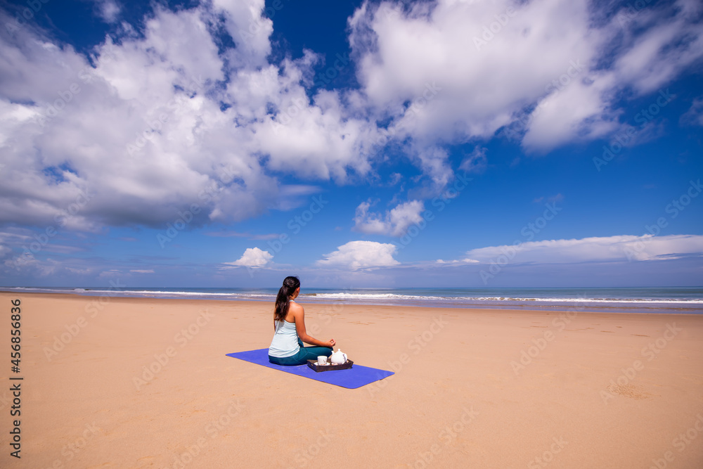 people and leisure concept- back view of woman meditating and drinking tea on the tropical beach with blue sky vackground people and leisure concept- back view of woman meditating and drinking tea on the tropical beach with blue sky vackground