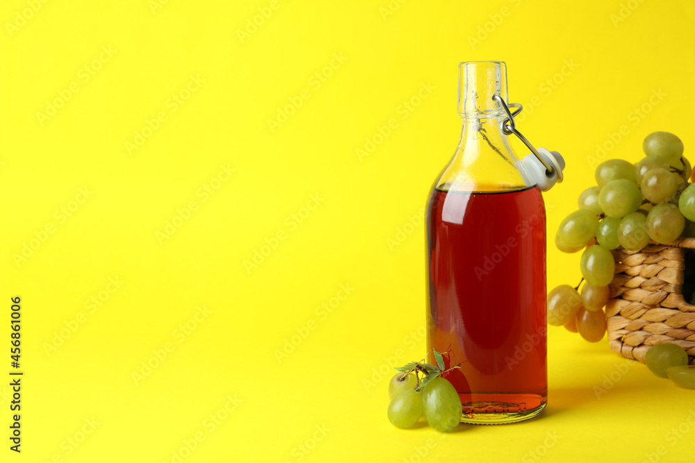 Bottle of vinegar and basket with grape on yellow background Bottle of vinegar and basket with grape on yellow background