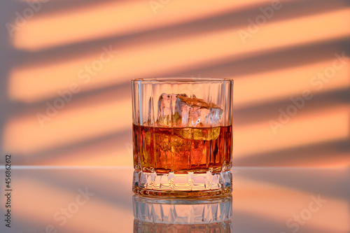 Whiskey with ice in rocks glass over striped background