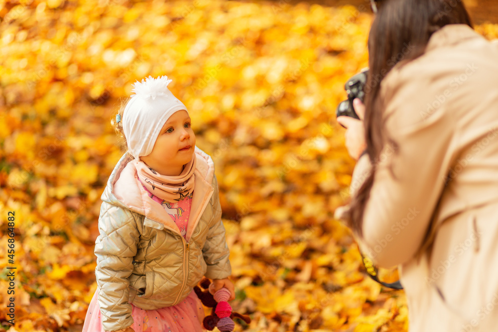 Woman mom photographer takes pictures of the child daughter in the autumn park with yellow foliage Woman mom photographer takes pictures of the child daughter in the autumn park with yellow foliage