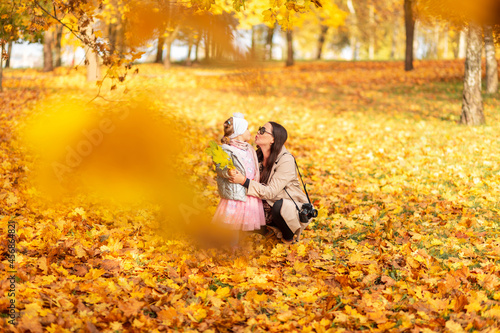 Mom with a baby daughter in stylish clothes with a camera kiss on the background of bright fall yellow foliage in the park. Family walk and photo session on golden autumn nature © alones