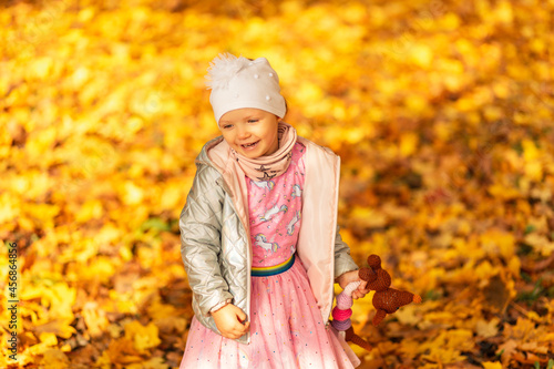 Happy beautiful girl child in fashionable clothes with a toy walks in the golden park with autumn yellow foliage