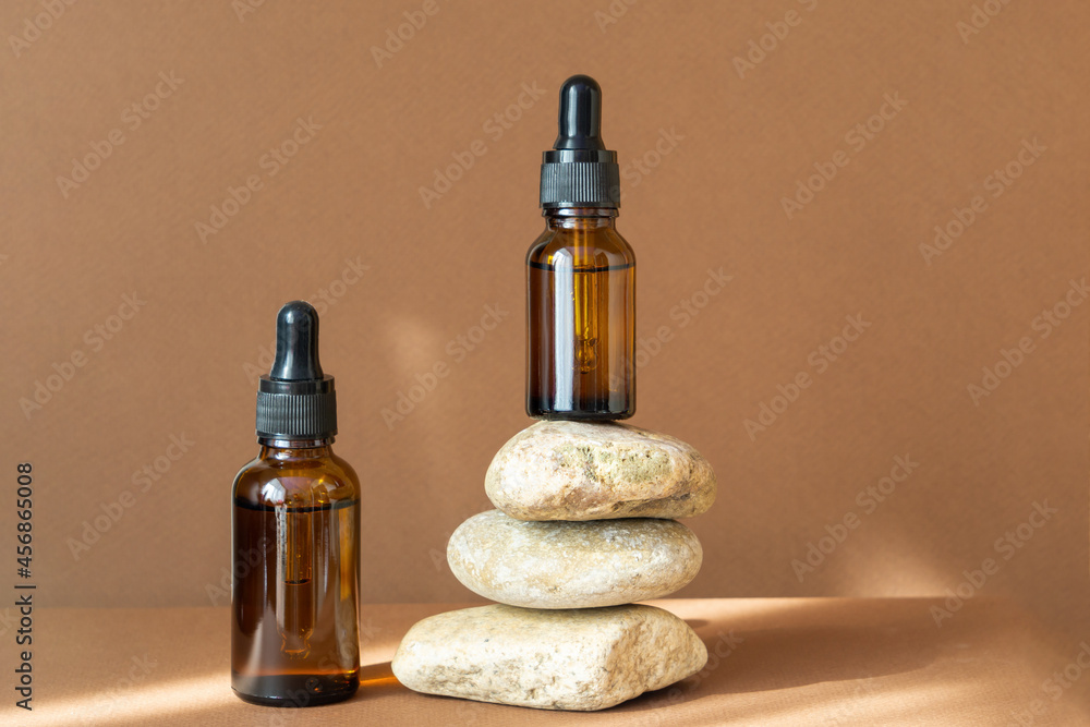 Mock up of two glass dropper bottles, one of which stands on stand made of natural stones, in rays of sunlight. Concept of body care, natural cosmetics Mock up of two glass dropper bottles, one of which stands on stand made of natural stones, in rays of sunlight. Concept of body care, natural cosmetics