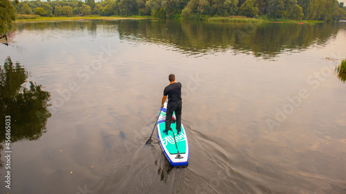 A man swims on a surfboard on a forest lake.