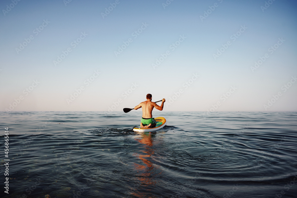 Back view of fit man floating on paddle board in the sea Back view of fit man floating on paddle board in the sea