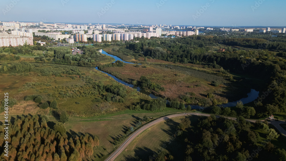 Fototapeta premium City landscape. Nearby there is a park area. Blue sky with white clouds. Aerial photography.