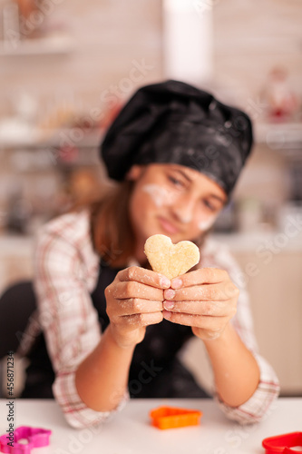 Portrait of smiling kid with apron holding traditional dough cooking gingerbread dessert in xmas culinary decorated kitchen. Grandchild baking homemade dessert at home celebrating christmas holiday