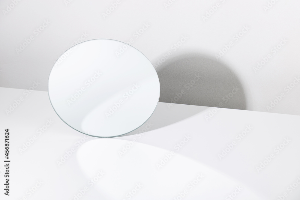 Minimalist mockup of round shaped mirror reflecting white wall placed on white table - obrazy, fototapety, plakaty 