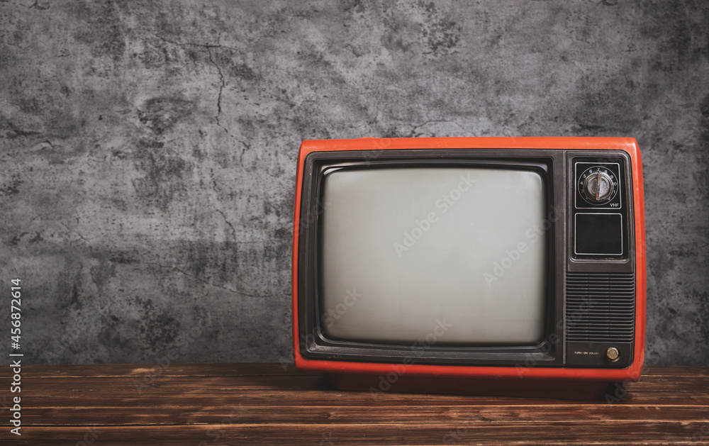 Retro old television on wooden table in front of concrete wall background, vintage TV filter effect.