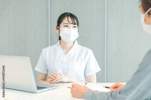 パソコンで受付する白衣の女性と患者 