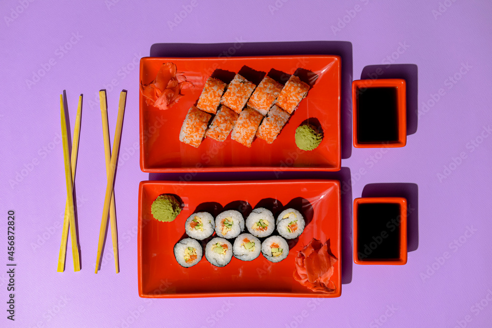 Japanese sushi rolls served on a red plate with pickled ginger and wasabi sauce over colorful purple background. Japanese sushi rolls served on a red plate with pickled ginger and wasabi sauce over colorful purple background.
