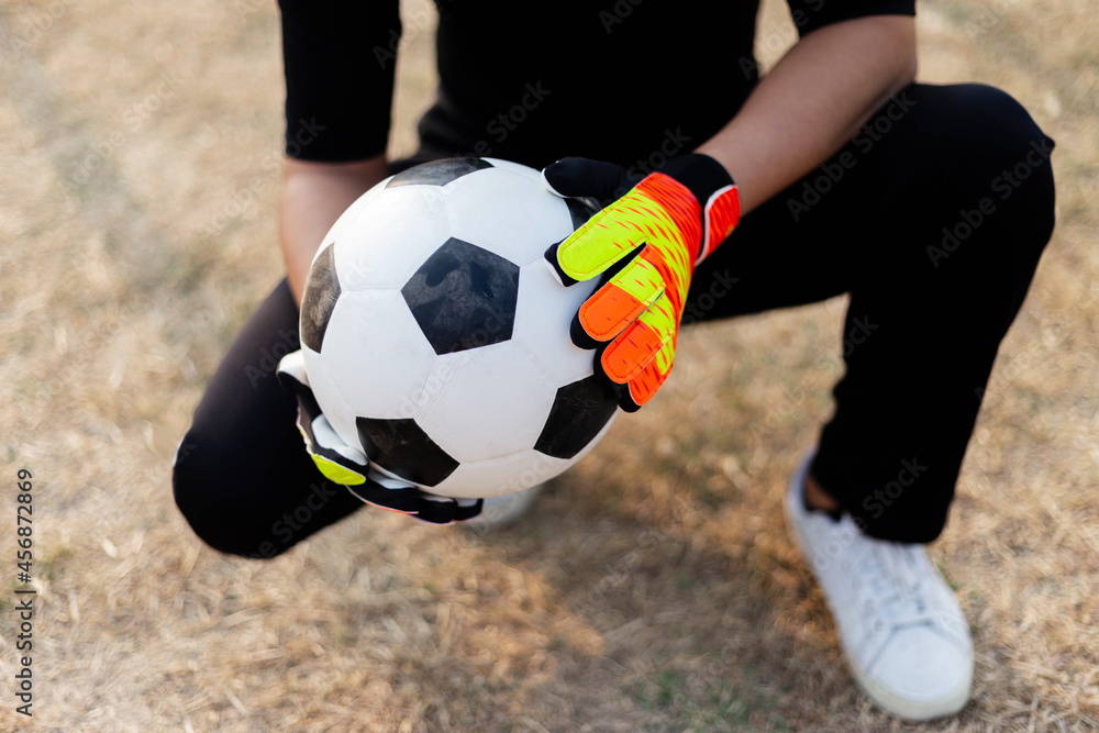 Sports and recreation concept a male teenage goalkeeper wearing black outfit and a pair of colorful gloves holding a soccer