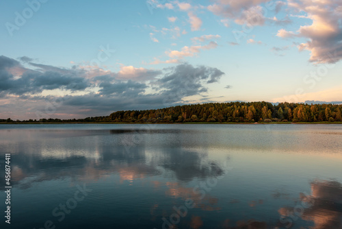 Landscape with a river and a forest illuminated by the setting sun. Reflection of clouds in the water.