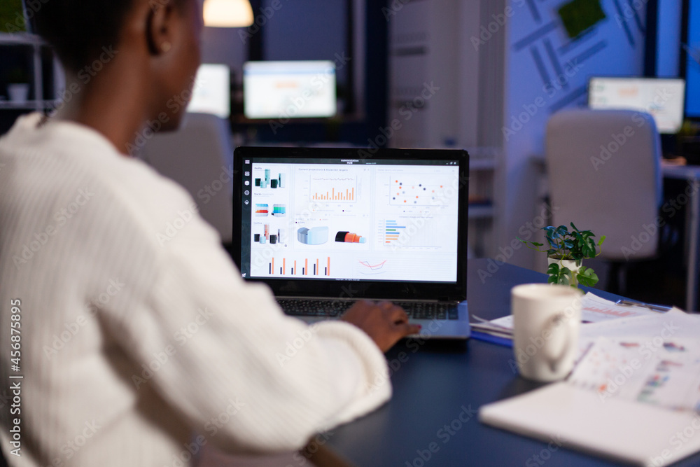 African american business entrepreneur analyzing financial company graphs on laptop computer overworking at annual reports late at night in startup office. Manager typing marketing statistics African american business entrepreneur analyzing financial company graphs on laptop computer overworking at annual reports late at night in startup office. Manager typing marketing statistics