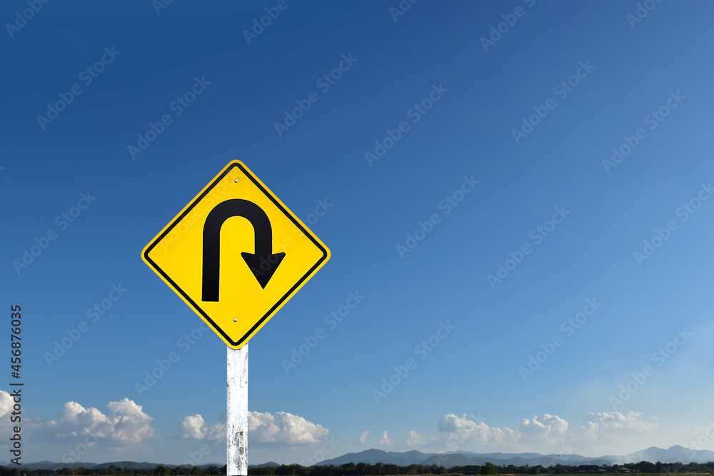 Traffic sign: Right U-turn sign on cement pole beside the rural road with white cloudy bluesky and landscape background, copy space.