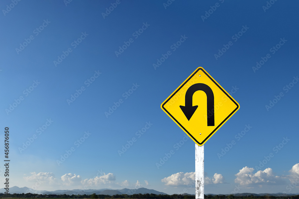 Traffic sign: Left U-turn sign on cement pole beside the rural road with white cloudy bluesky and landscape background, copy space. Traffic sign: Left U-turn sign on cement pole beside the rural road with white cloudy bluesky and landscape background, copy space.