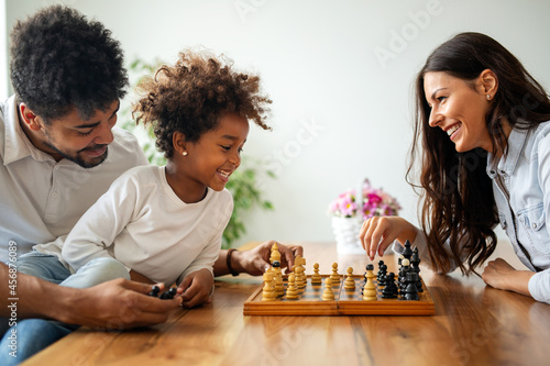 Parents and child playing chess while spending time together at home. Family love education concept
