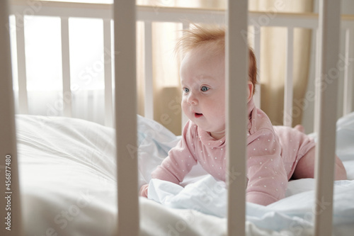 Cute baby girl crowling on white linen in her cradle after sleep photo