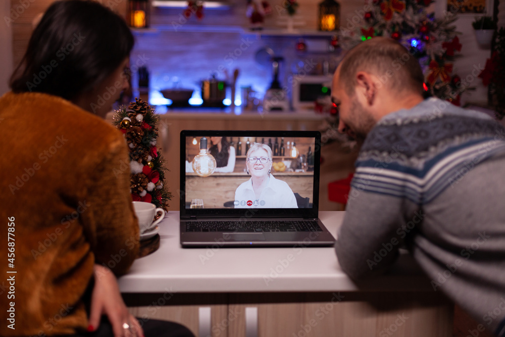 Happy family discussing with remote grandparent during online videocall conference celebrating christmas holiday together in xmas decorated kitchen. Joyful couple enjoying winter season