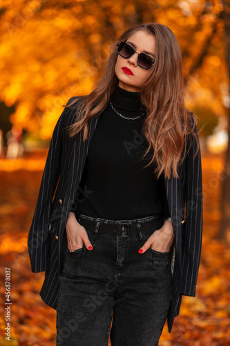 beautiful young business woman with sunglasses in a stylish suit with a fashionable blazer walks in an autumn park with an orange leaves