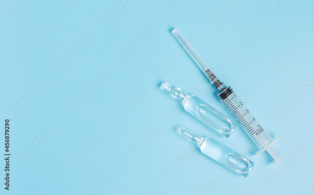 Disposable syringe and two glass ampoules on a blue background. Copy space. Disposable syringe and two glass ampoules on a blue background. Copy space.