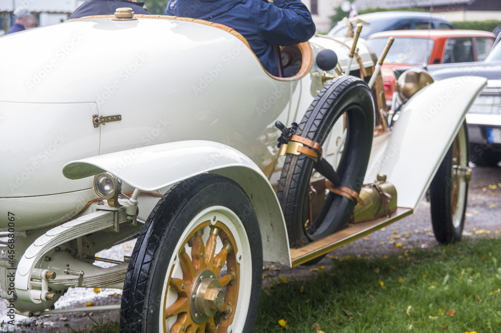 Close-up of elegant refined white gold antique retro sport renovated car 1914 on exhibition. Man driving in old vintage classic automobile with umbrella, opened motor, wooden wheels, cool horn