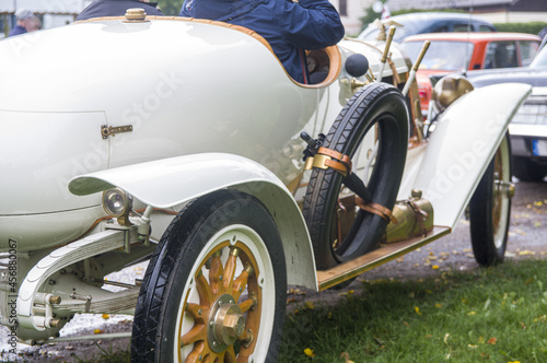 Close-up of elegant refined white gold antique retro sport renovated car 1914 on exhibition. Man driving in old vintage classic automobile with umbrella, opened motor, wooden wheels, cool horn