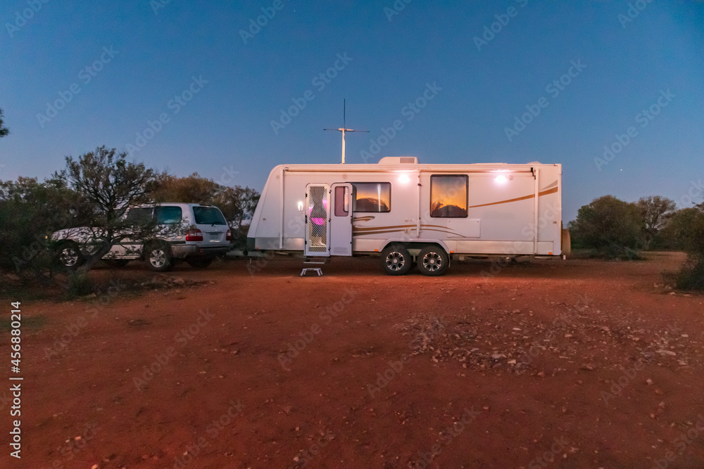 A large white caravan and four wheel drive vehicle parked in the outback of Australia at dusk.