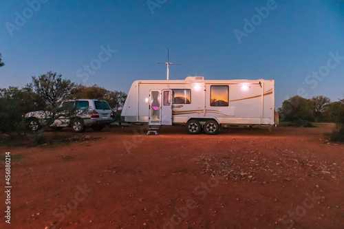 A large white caravan and four wheel drive vehicle parked in the outback of Australia at dusk.