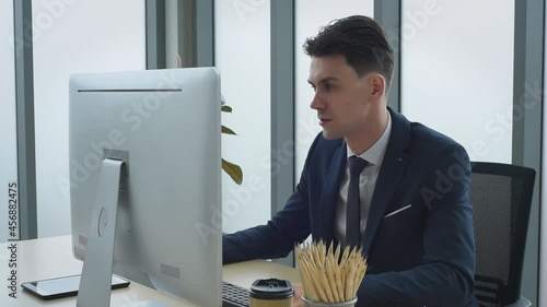 Handsome business man in suit outfit working in front of computer with smart and confident typing on keyboard in modern office
