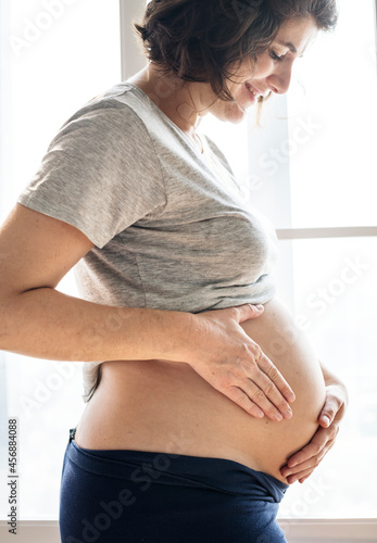 Cheerful pregnant woman standing by the window