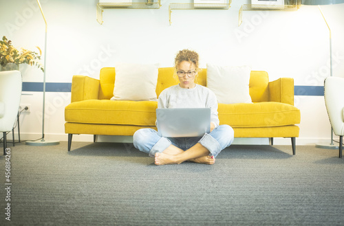 Young woman at home sitting on floor with crossed legs working or studying using laptop in the living room at home. Woman sitting on living room floor working on laptop at home office