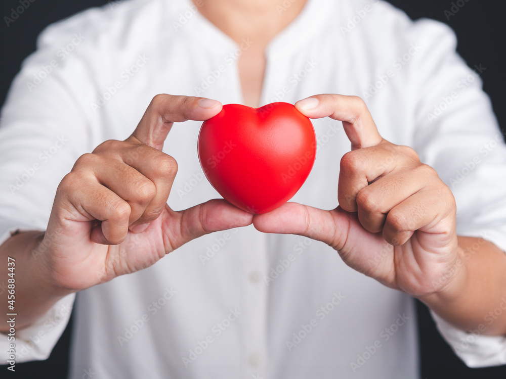Hand of a holding a red heart shape while standing with a black background in the studio. Close-up photo. Space for text. Donate, love, and encouragement concept Hand of a holding a red heart shape while standing with a black background in the studio. Close-up photo. Space for text. Donate, love, and encouragement concept
