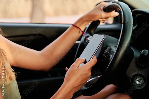 Close-up of a woman's hands driving while using her smart phone. Concept of traffic education and traffic accidents. © Alvaro