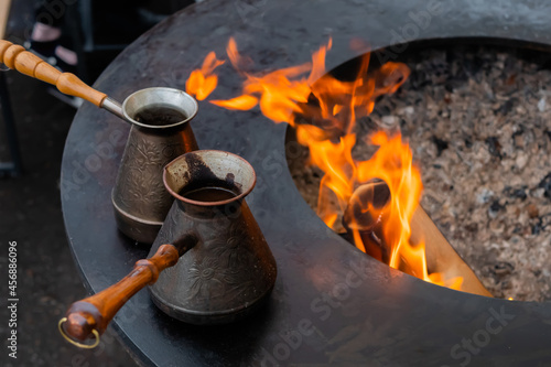 Preparing Turkish coffee with black cezve or ibrik - traditional coffee pot on outdoor round brazier with hot flame at street food festival - close up photo