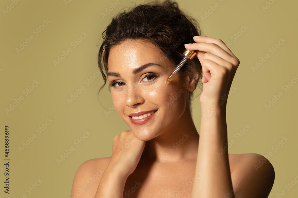 Beautiful young female moisturizing glowing facial skin by serum collagen and hyaluronic acid. Hands with serum dropper near girl face. Skincare and rejuvenation cosmetics for natural woman beauty. Beautiful young female moisturizing glowing facial skin by serum collagen and hyaluronic acid. Hands with serum dropper near girl face. Skincare and rejuvenation cosmetics for natural woman beauty.