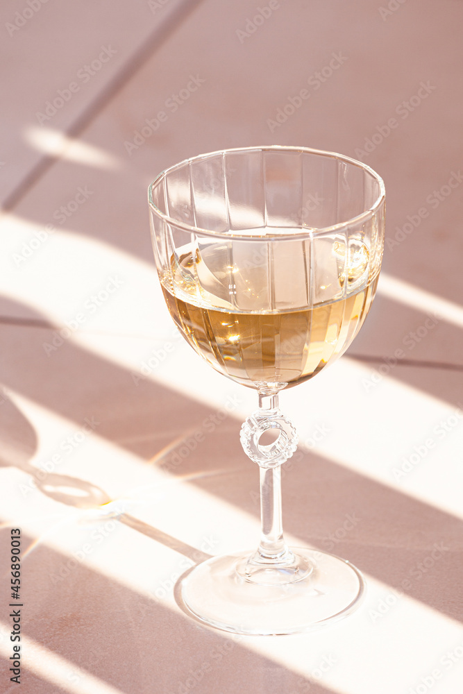 glass of white wine on tiles with shadows outdoor on terrace summer day