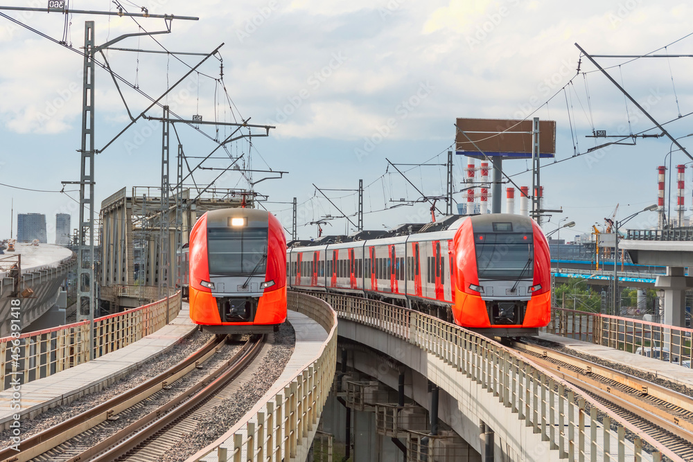 Two electric passenger train drives at high speed among urban landscape. Two electric passenger train drives at high speed among urban landscape.